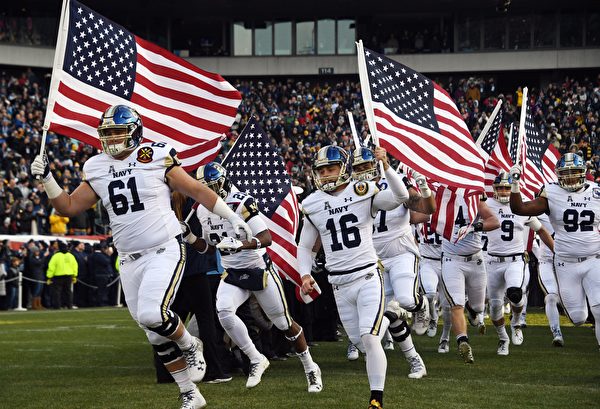 TOPSHOT - Players of the Navy Midshipmen of the US Naval Academy (USNA) arrive waving the American flag prior to the annual Army-Navy football game at Lincoln Financial Field in Philadelphia, Pennsylvania, December 8, 2018. - US President Donald Trump  will officiate the coin toss between the Army Black Knights of the US Military Academy (USMA) and the Navy Midshipmen of the US Naval Academy (USNA). (Photo by Jim WATSON / AFP)        (Photo credit should read JIM WATSON/AFP/Getty Images)