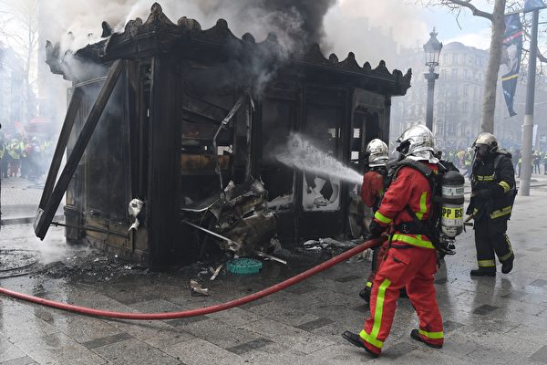 3月16日，巴黎香街上被黄背心示威者烧毁的法国传统式售报亭。图为消费员正在灭火（ALAIN JOCARD/AFP/Getty Images）