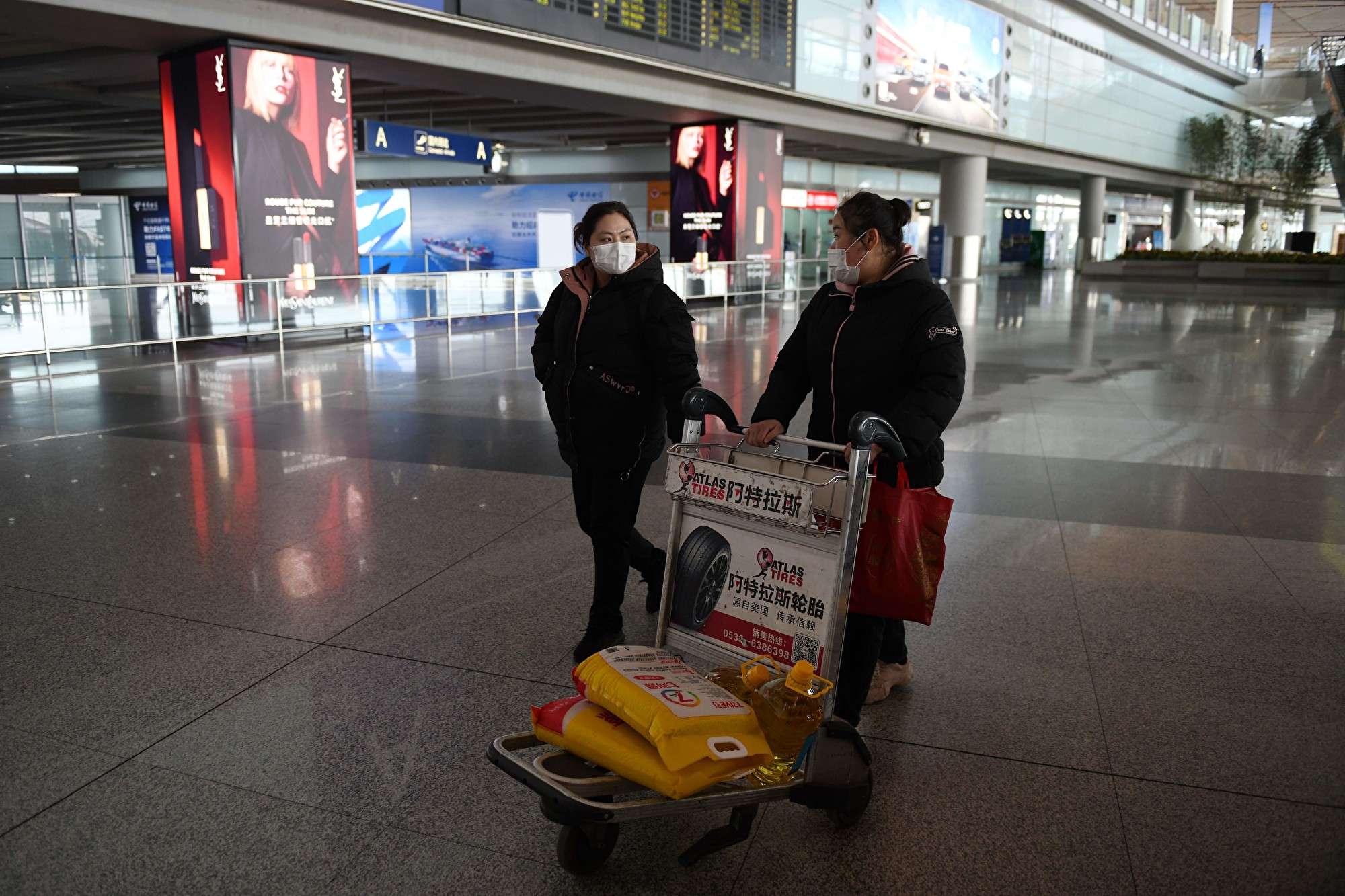 3月27日北京首都机场内，2名女子推着一部载有米和油的手推车。(GREG BAKER/AFP)
