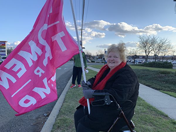珍妮絲·托馬斯（Janice Thomas）是一位殘疾的婦女，她每周六都來此支持特朗普總統。她舉著一面「Women For Trump」（婦女支持特朗普）的粉紅色旗幟。（郭茗／大紀元）