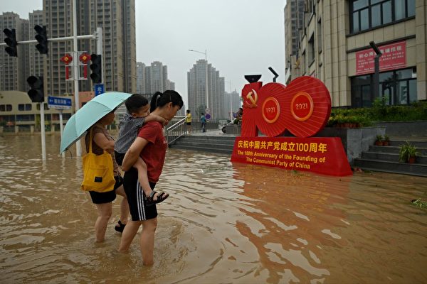 7月23日，郑州民众走过大水淹没的街道，旁边是中共党庆的标志。（Noel Celis/AFP via Getty Images）