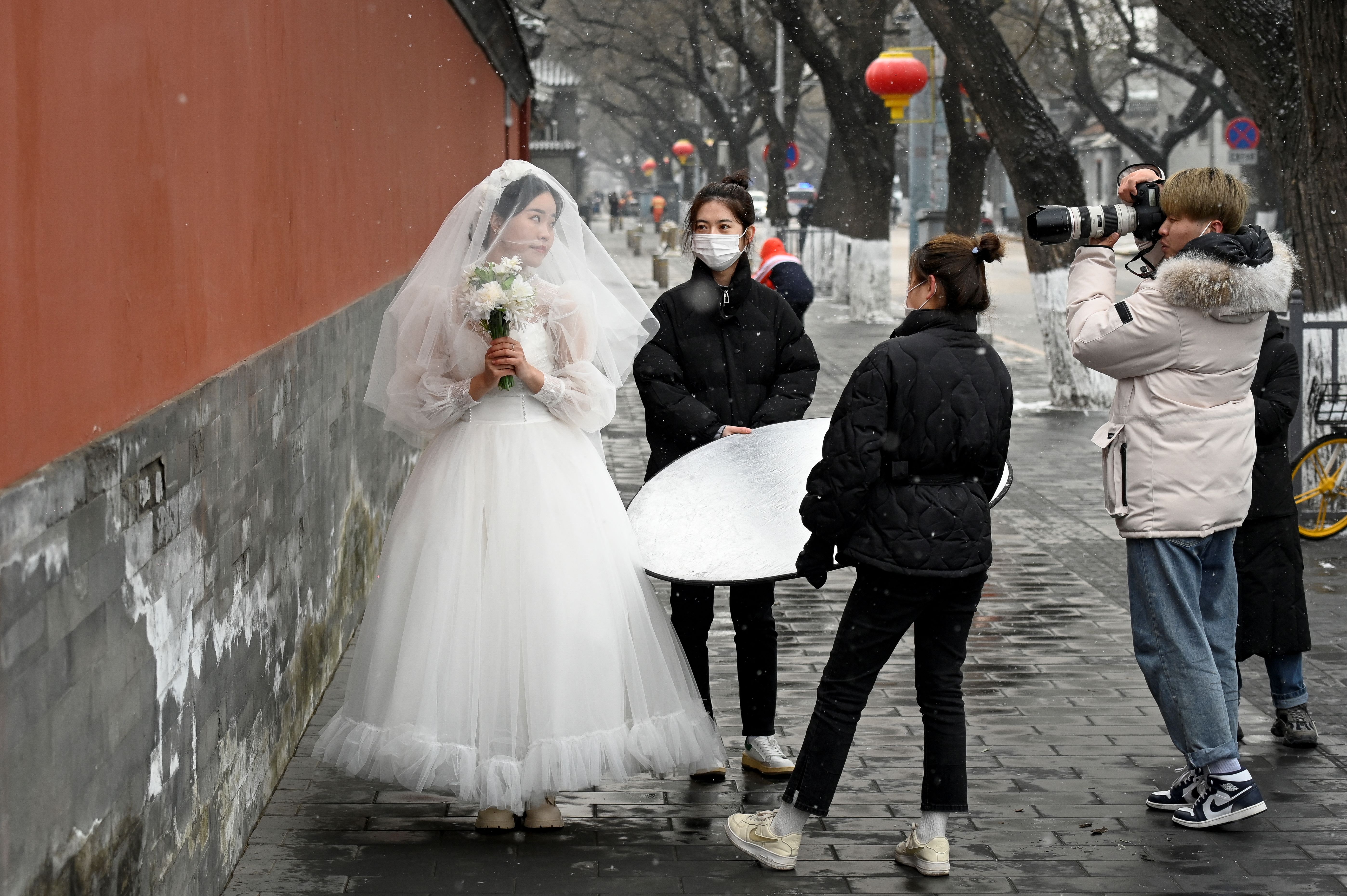 中国低迷的经济状况不仅让很多普通年轻人对结婚生畏,就连较富有的年轻人也表示,担心承担不起结婚成本。图为2022年1月20日,北京,一位女士(左)在故宫外拍婚纱照。(Wang Zhao/AFP)