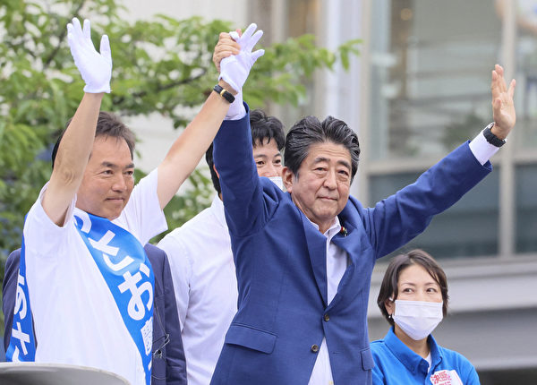2022年7月6日，日本前首相安倍晋三（中）被暗杀前2天，在东京郊区与自民党候选人麻生敬一郎共同举起双臂向支持者示意。（Yoshikazu Tsuno/AFP via Getty Images）
