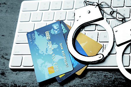 Credit cards and handcuffs on computer keyboard, closeup