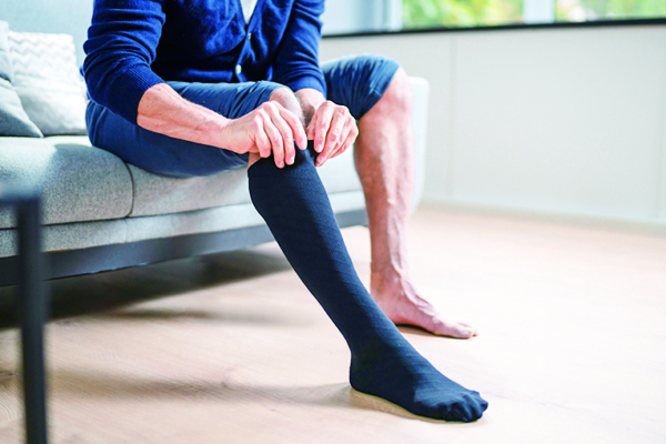 Man Putting On Medical Compression Stockings On Legs