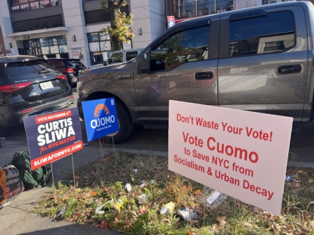 人行道上插著三位市長候選人的廣告牌。