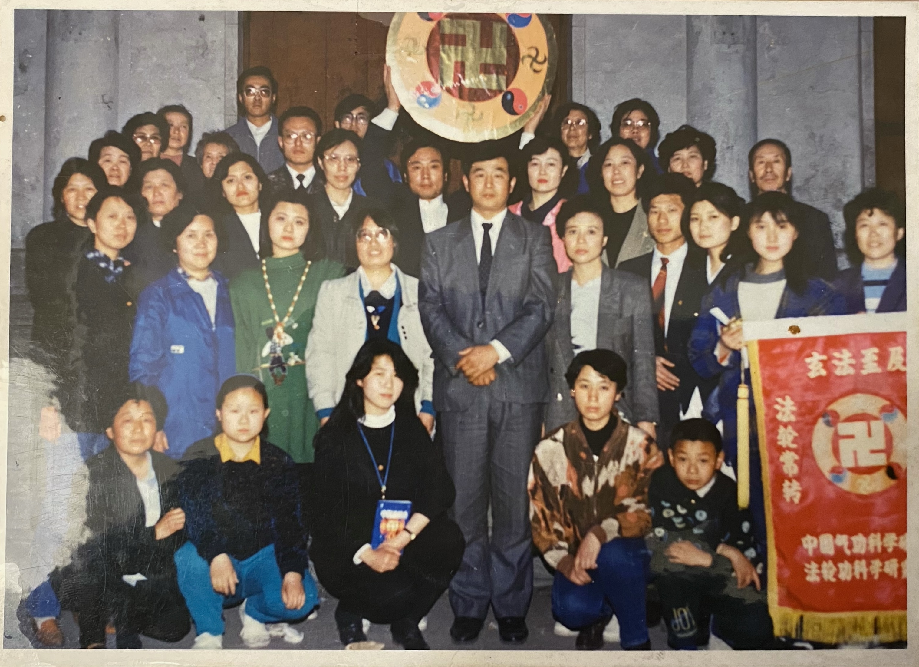 李洪志先生(中间穿西服者)1993年4月29日—5月8日在吉林大学举办长春第七期传功讲法班,学习班结束时,与学员合影。张泽夫妇站在师父身后,张泽高高地举着法轮图形。(张泽提供)