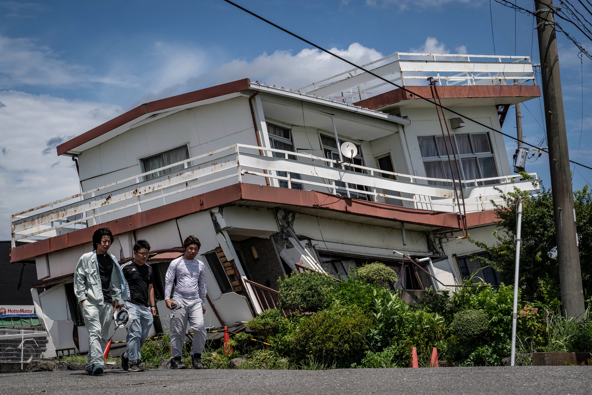 2026年7月29日,日本熊本縣八代市,幾名工人走過一棟在地震中嚴重受損的房屋。(Yuichi Yamazaki/AFP via Getty Images)