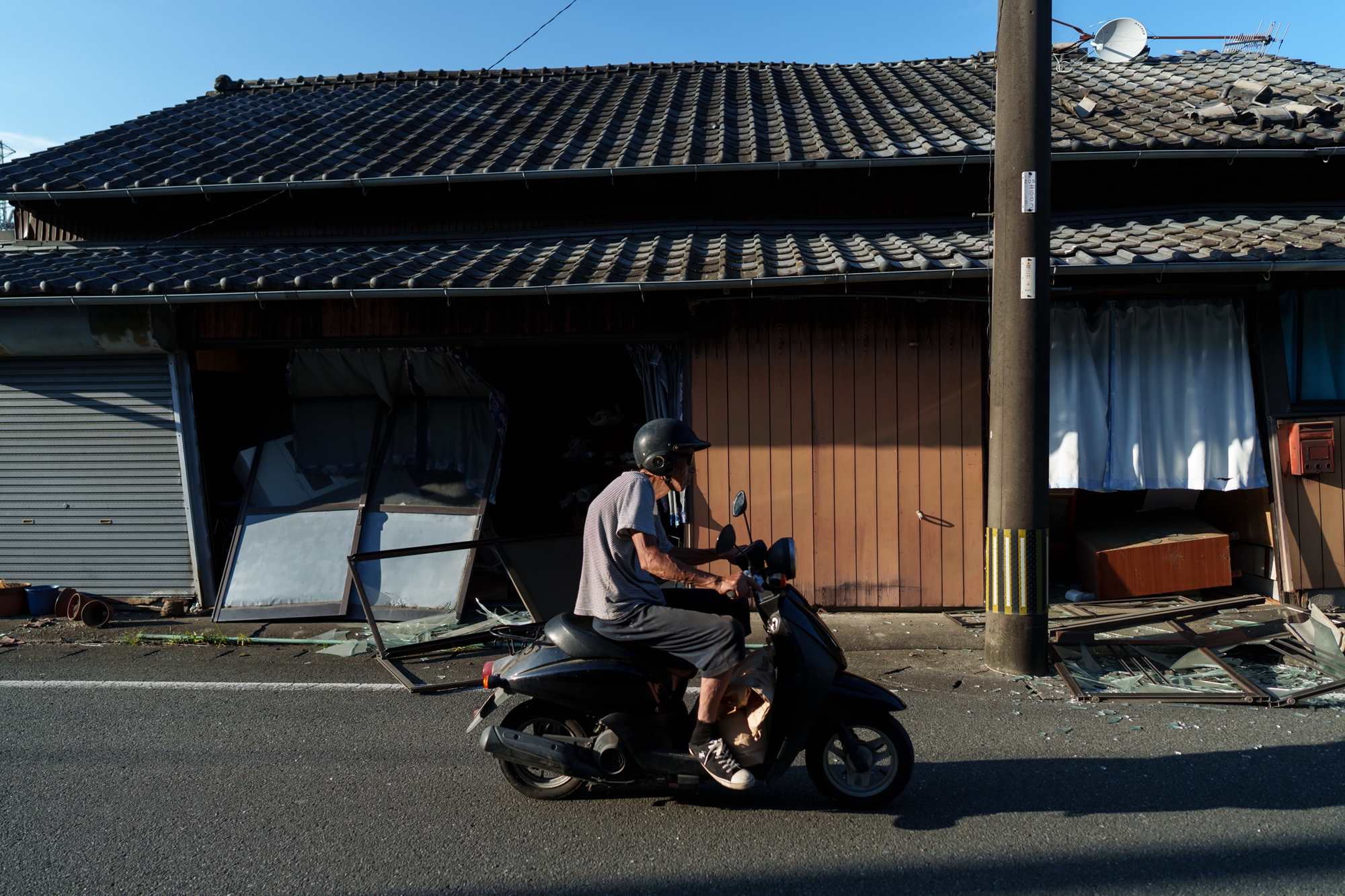 2026年7月29日,日本熊本縣八代市,一名男子騎車經過一棟受損的房屋。(Tomohiro Ohsumi/Getty Images)