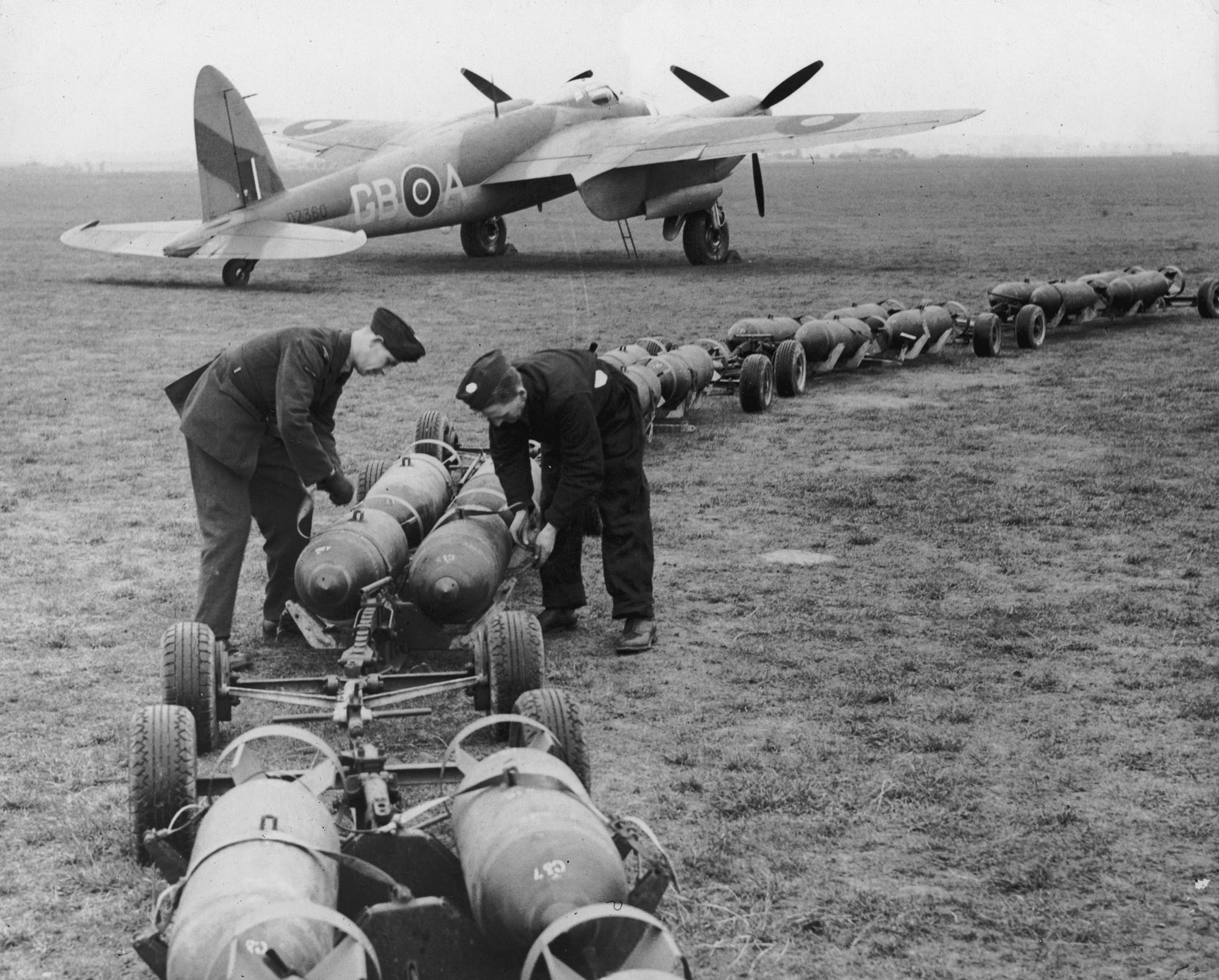 約1942年,一架「蚊」式戰鬥機停放在英國空軍基地內,地勤人員正從「炸彈列車」上卸載炸彈。(Hulton Archive/Getty Images)