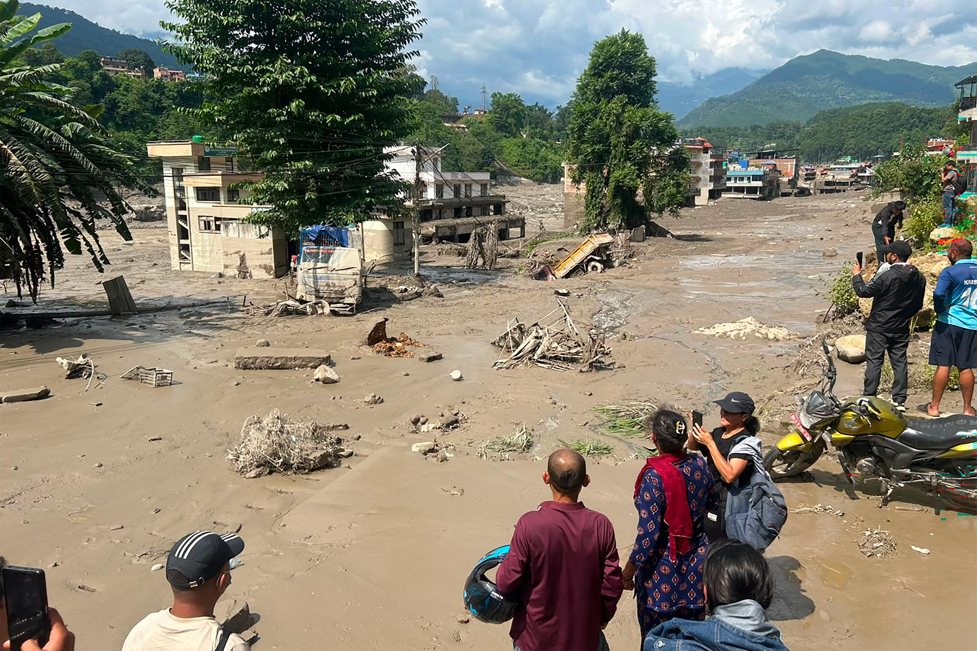 2026年8月26日,尼泊爾努瓦科特縣(Nuwakot)特里蘇里巴扎爾(Trishuli Bazar)發生山洪,河岸邊房屋部分被泥水掩埋,居民們聚在路邊觀看。(Prakash Mathema/AFP via Getty Images)