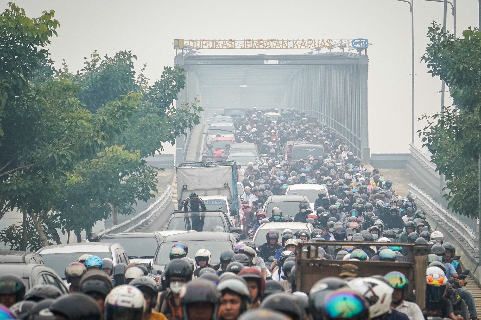 2026年10月7日,位於西加里曼丹省坤甸市(Pontianak)的卡普阿斯第一大橋複線橋(Duplikasi Jembatan Kapuas 1)籠罩在一片煙霾之中,許多民眾戴著口罩經過此地。(Dito/AFP via Getty Images)